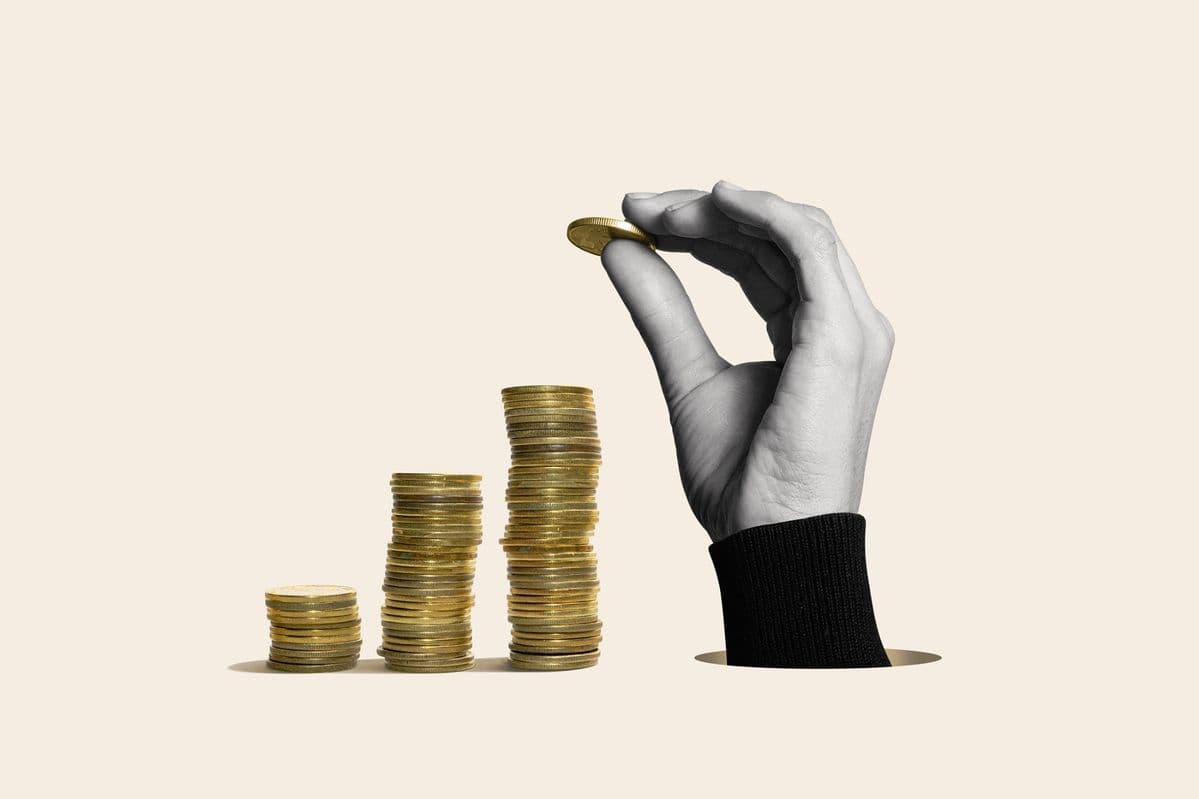 Una mano coloca una moneda sobre pilas de monedas de tamaño creciente